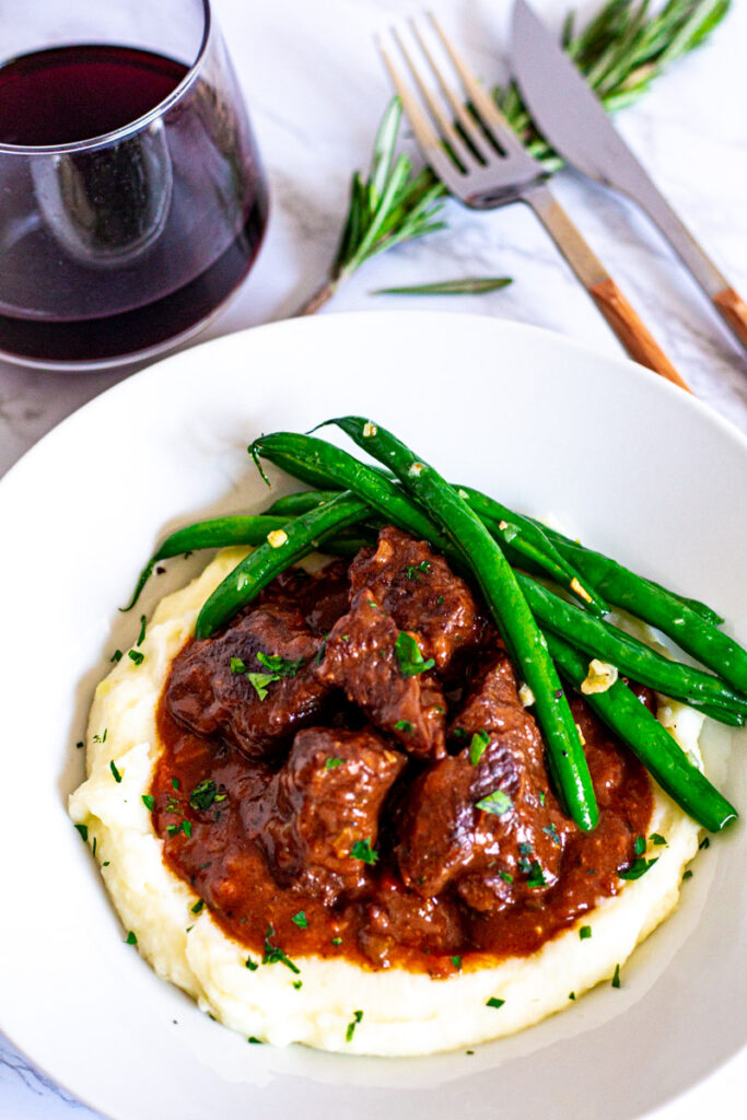 Overhead shot of brandy braised beef on the bed of mashed potato with green beans on the side.