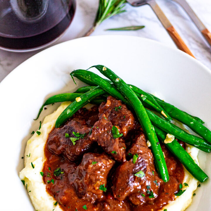 Overhead shot of brandy braised beef on the bed of mashed potato with green beans on the side.