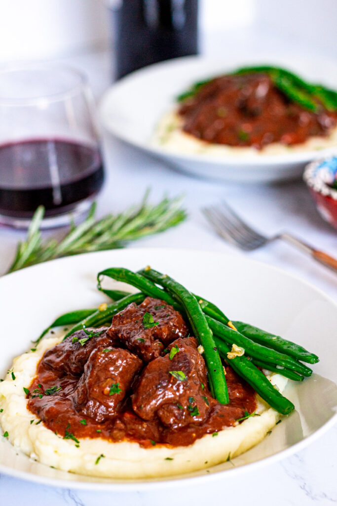 Two plates of brandy braised beef with mashed potato and sauteed green beans.