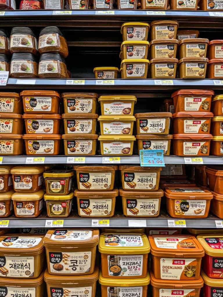 Shelf of Korean doenjang (fermented soybean paste) from various brands including Sempio, Haechandle, and O’Food