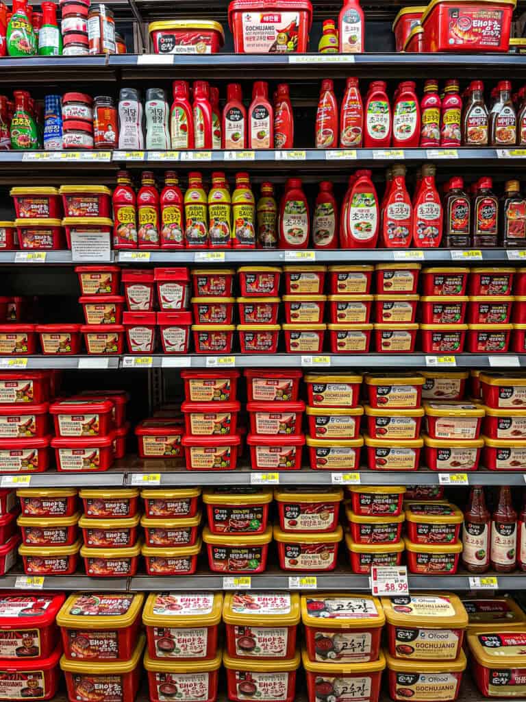 A full shelf of Korean gochujang red pepper paste from brands like Haechandle, O’Food, and Chung Jung One