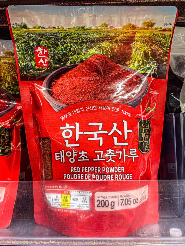 A vivid red package of sun-dried Korean gochugaru with a field background image, labeled for authentic taste and rich heat level
