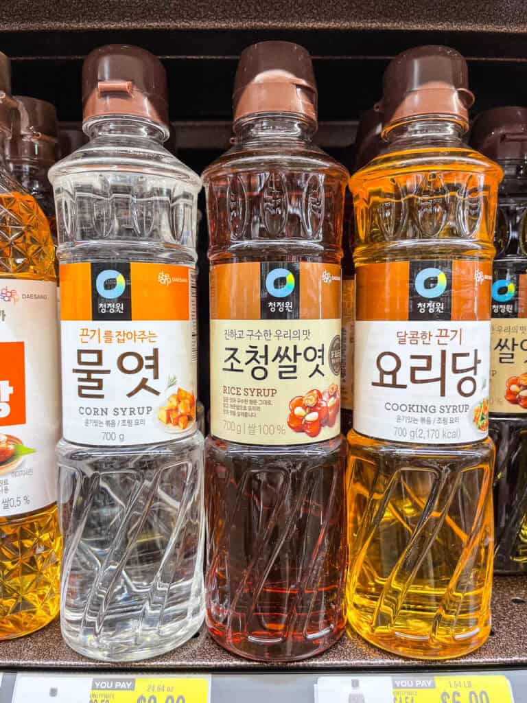 Three bottles of Korean syrup—corn syrup, rice syrup, and cooking syrup—lined up on a grocery shelf