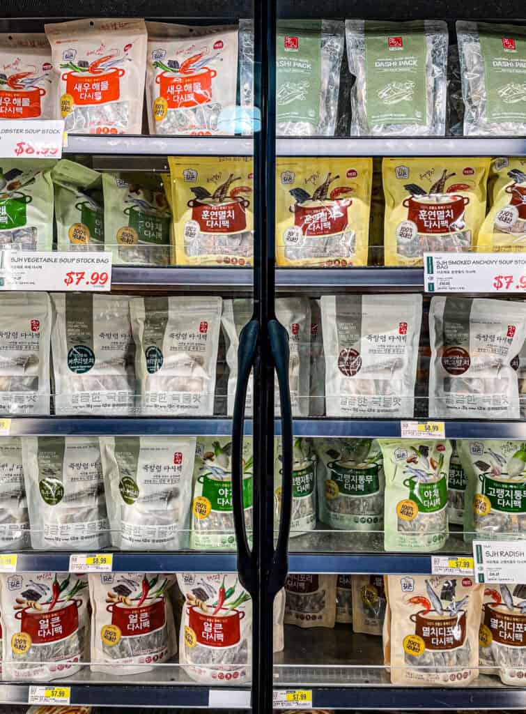 Refrigerated section with assorted Korean soup stock bags, including anchovy, shrimp, vegetable, and radish-based pouches for convenient broth-making