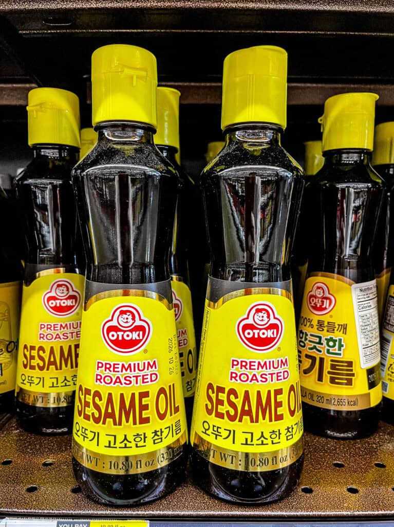 Two bottles of Ottogi Premium Roasted Sesame Oil with yellow caps displayed on a store shelf