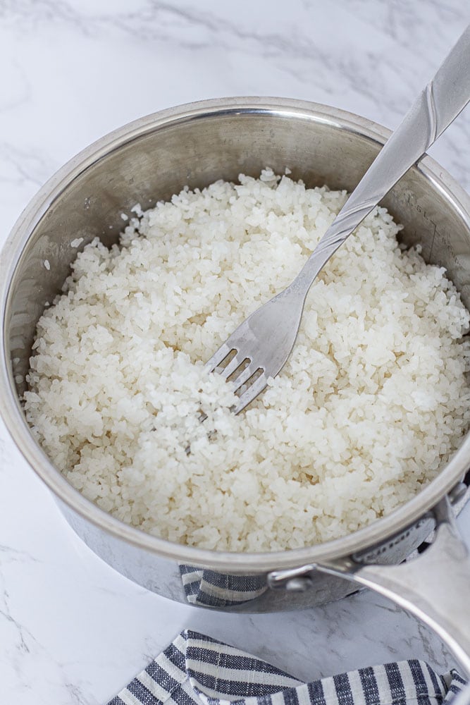 Fluffy broken jasmine rice in a pot fluffed with a fork after cooking