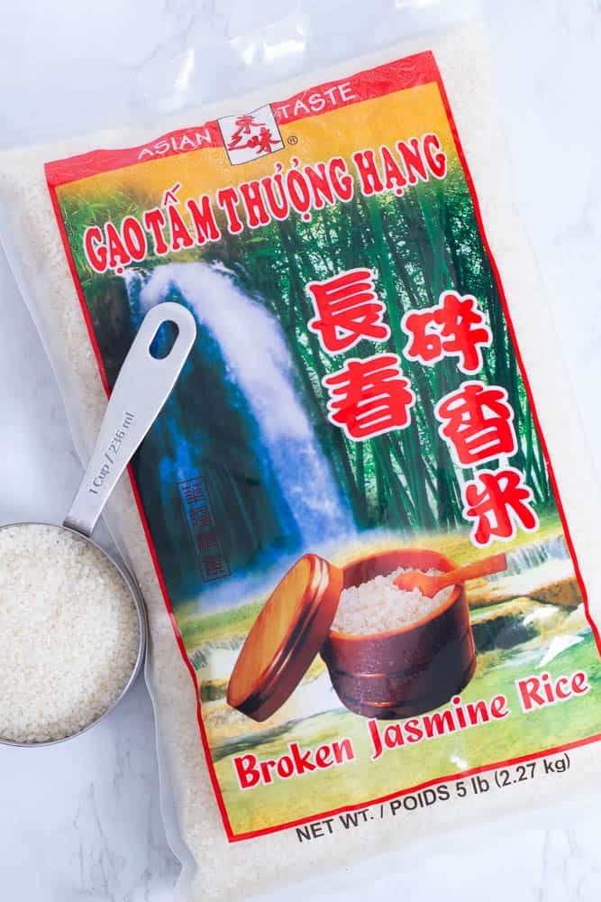 Broken jasmine rice product bag with a measuring cup of rice on marble surface