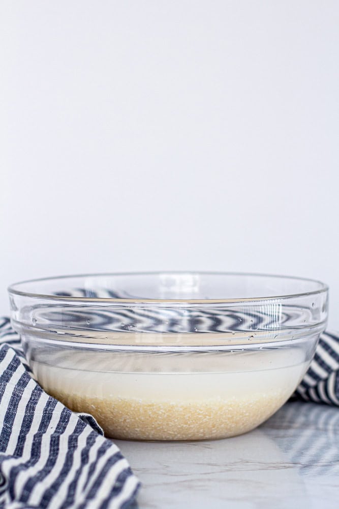 Unrinsed broken jasmine rice in a glass bowl showing cloudy starch water before cooking