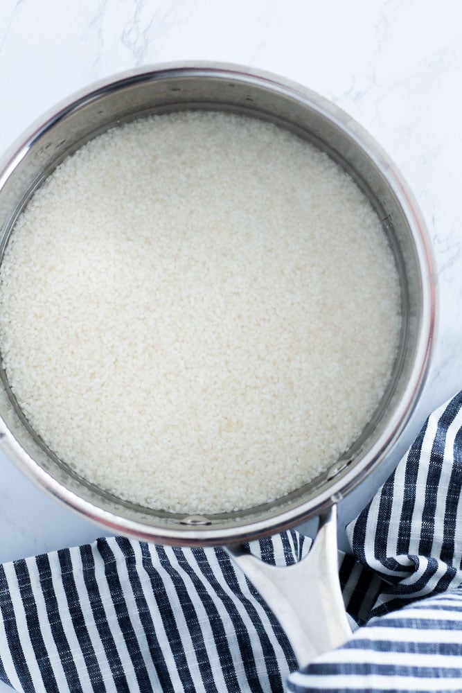 Broken jasmine rice with water in a stainless steel pot before cooking on the stovetop