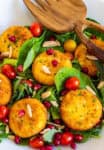 Top view of fried goat cheese salad with tomatoes, pomegranate seeds, and wooden salad tongs