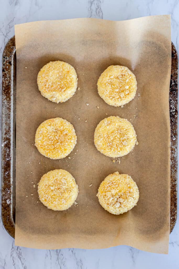 Six breaded goat cheese rounds on a parchment-lined baking sheet, ready to be fried