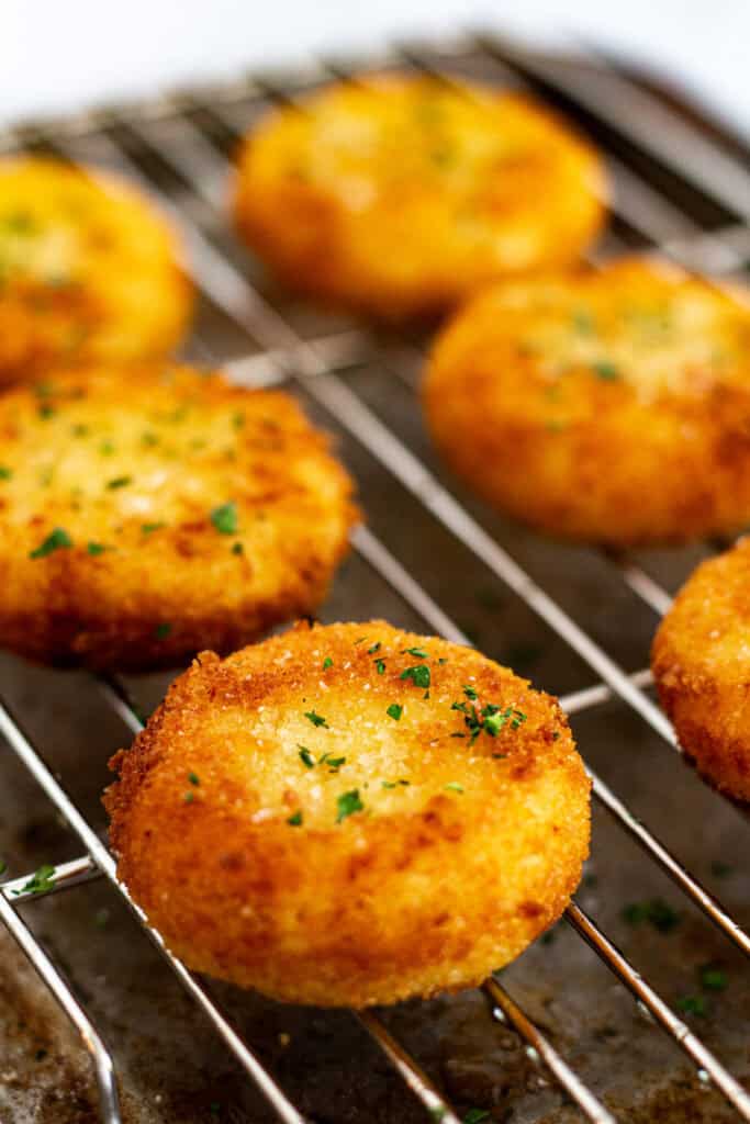 Close-up of golden brown fried goat cheese rounds sprinkled with parsley on wire rack