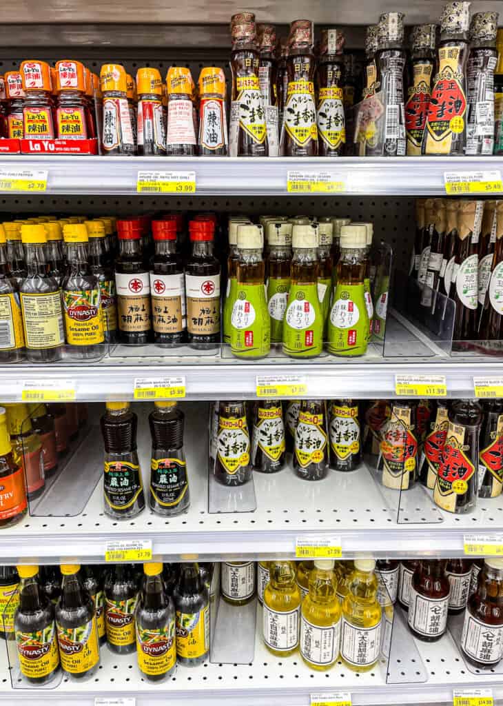 Assorted bottles of toasted and pure sesame oil on a grocery store shelf, a key ingredient in Japanese cooking.
