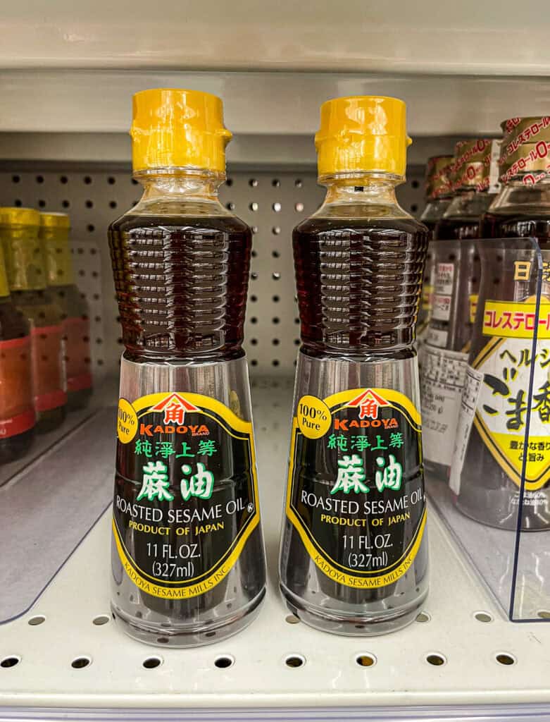 Close-up of Kadoya brand roasted sesame oil bottles on a grocery store shelf, a fragrant and flavorful oil used in Japanese cuisine.
