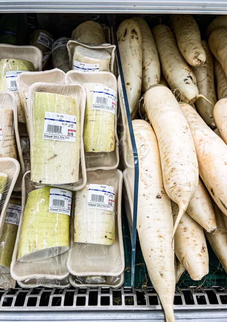 Whole and cut fresh daikon radishes on display in a grocery store, a versatile root vegetable used in Japanese cooking.