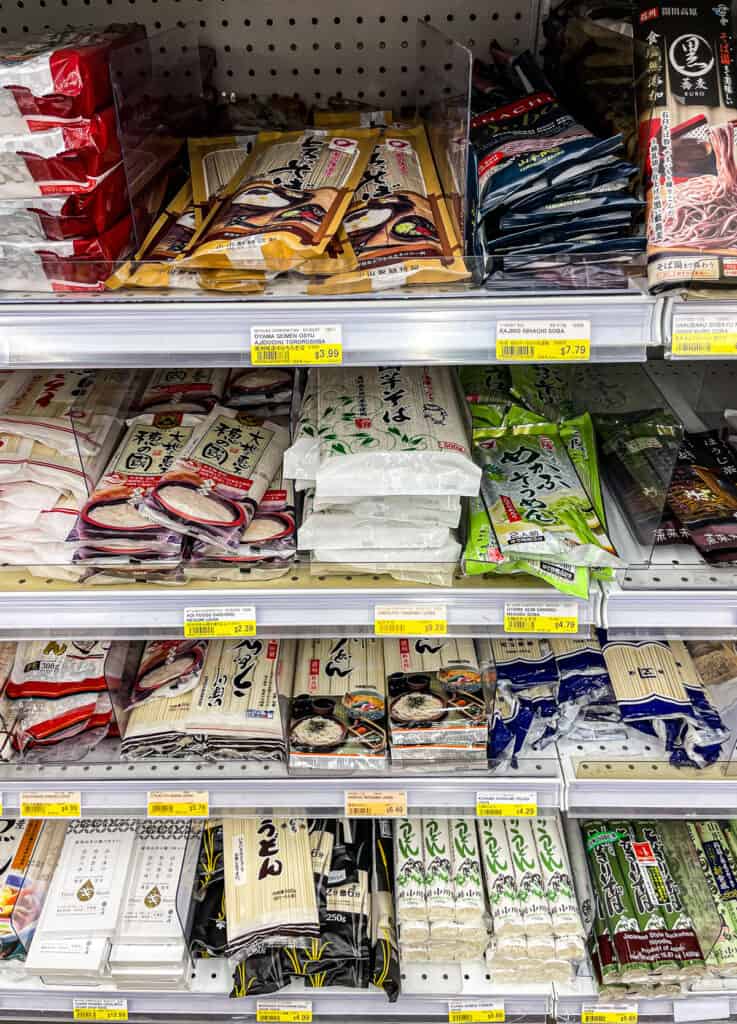 Assorted packages of Japanese dried noodles including soba, udon, and somen displayed on a grocery store shelf.