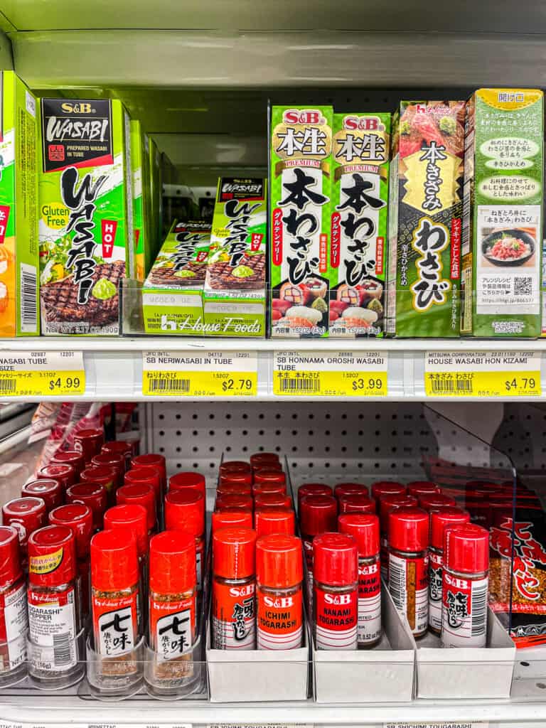 Grocery shelf stocked with tubes of wasabi paste and bottles of shichimi togarashi, essential Japanese condiments for adding heat and flavor.