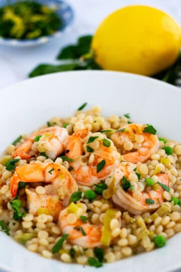 Bowl of couscous risotto with shrimp and leeks, garnished with parsley and lemon zest