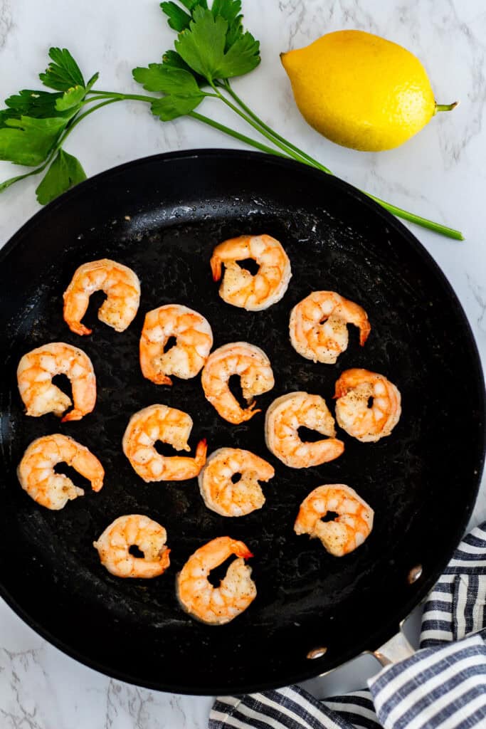 Searing shrimp in a black pan with parsley and lemon for couscous risotto with shrimp and leeks