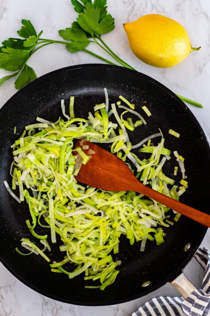 Thinly sliced leeks sautéing in a pan for creamy couscous risotto with shrimp and leeks