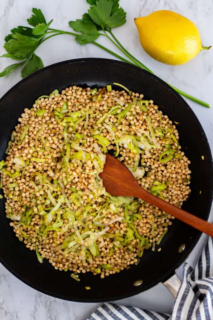 Israeli couscous toasted with leeks in a black skillet to build flavor for couscous risotto