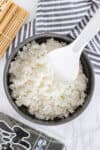 Seasoned sushi rice in a bowl with a rice paddle, ready to roll with nori sheets and bamboo mat nearby