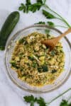 Bowl of zucchini couscous with garam masala, scallions, and parsley with a wooden spoon