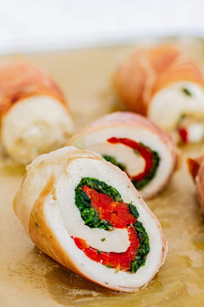 Sliced chicken roulade showing spinach and roasted red pepper filling wrapped in prosciutto.