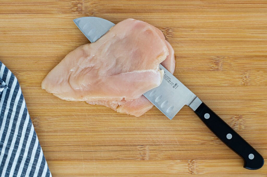 Chicken breast on a cutting board being sliced open with a knife for chicken roulade preparation.