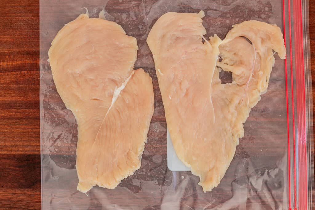Two pounded chicken breasts side by side on a plastic bag, prepared for chicken roulade filling.