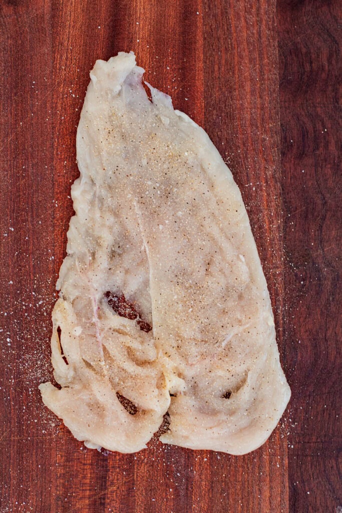 Pounded chicken breast seasoned on a cutting board.