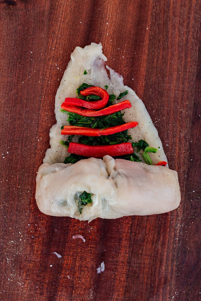 Chicken breast being rolled around a spinach and roasted red pepper filling.