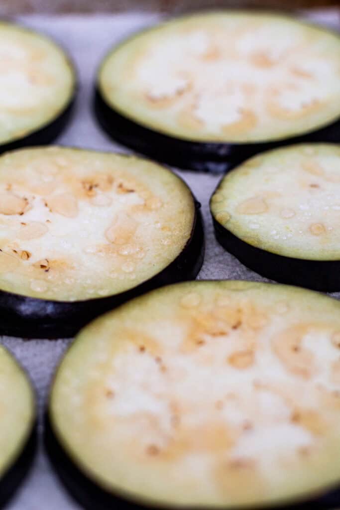 Close-up of salted eggplant slices with water beads on surface, showing how salting draws out moisture before roasting