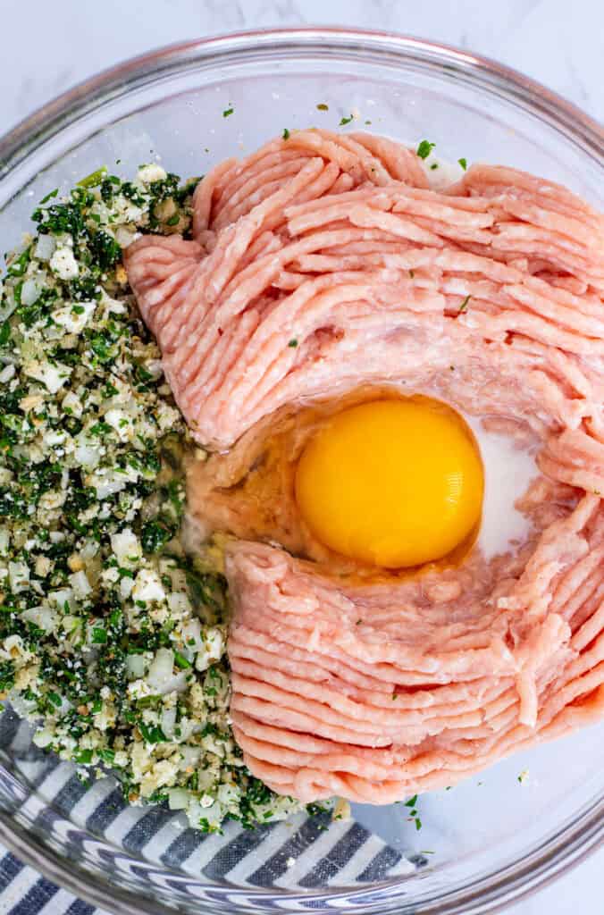 Ground chicken, milk and egg added to bowl of feta, onion, and herbs for healthy Greek chicken meatballs