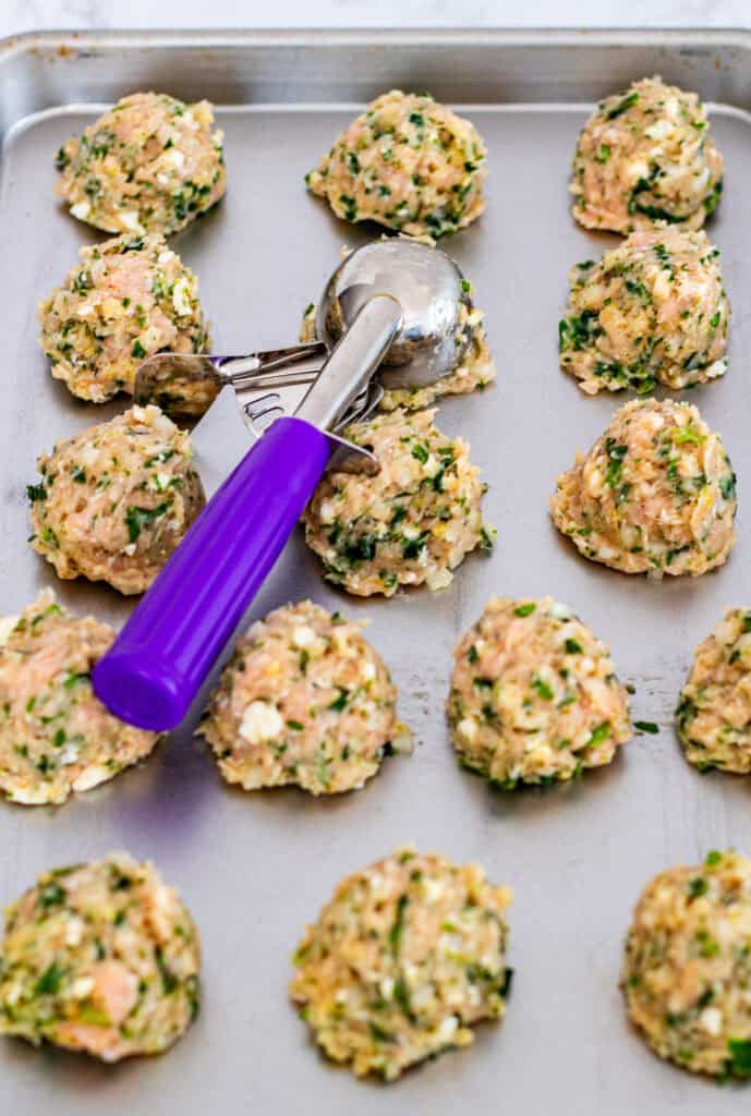 Chicken meatball mixture with feta and herbs being scooped onto a baking sheet