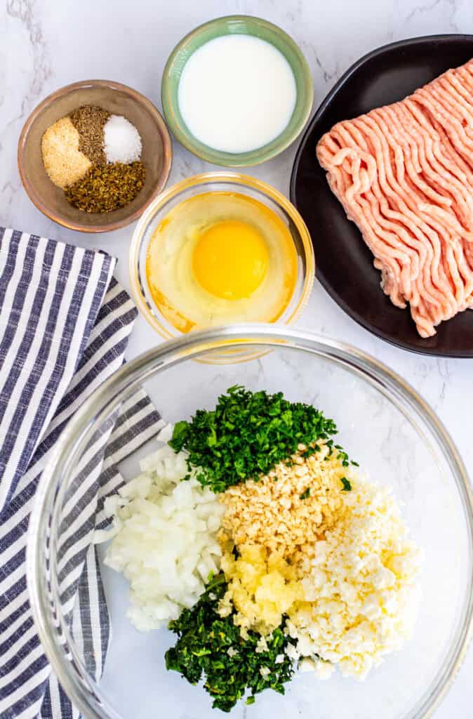 Ingredients for Greek chicken meatballs with feta including ground chicken, garlic, onion, fresh herbs, feta cheese, egg, and spices