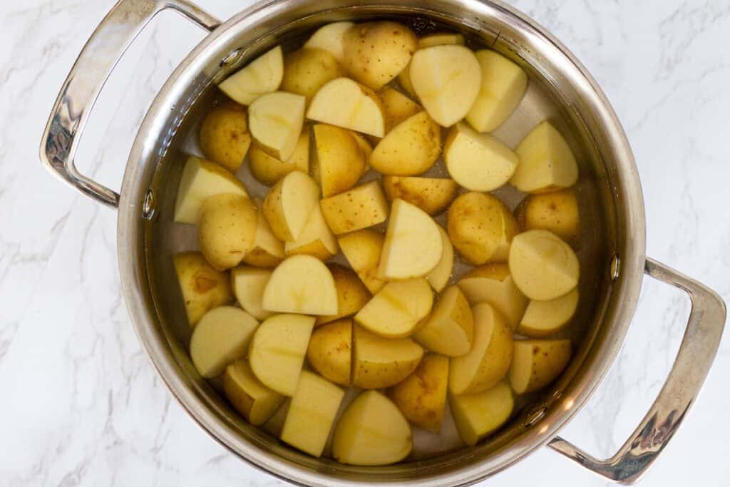 Diced yellow potatoes in a pot of salted water, ready to be boiled for herb roasted potatoes.