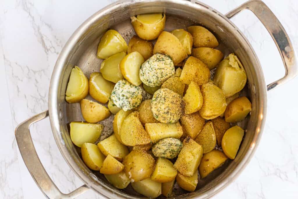 Cooked yellow potatoes tossed with herb butter, garlic powder, and black pepper before roasting.