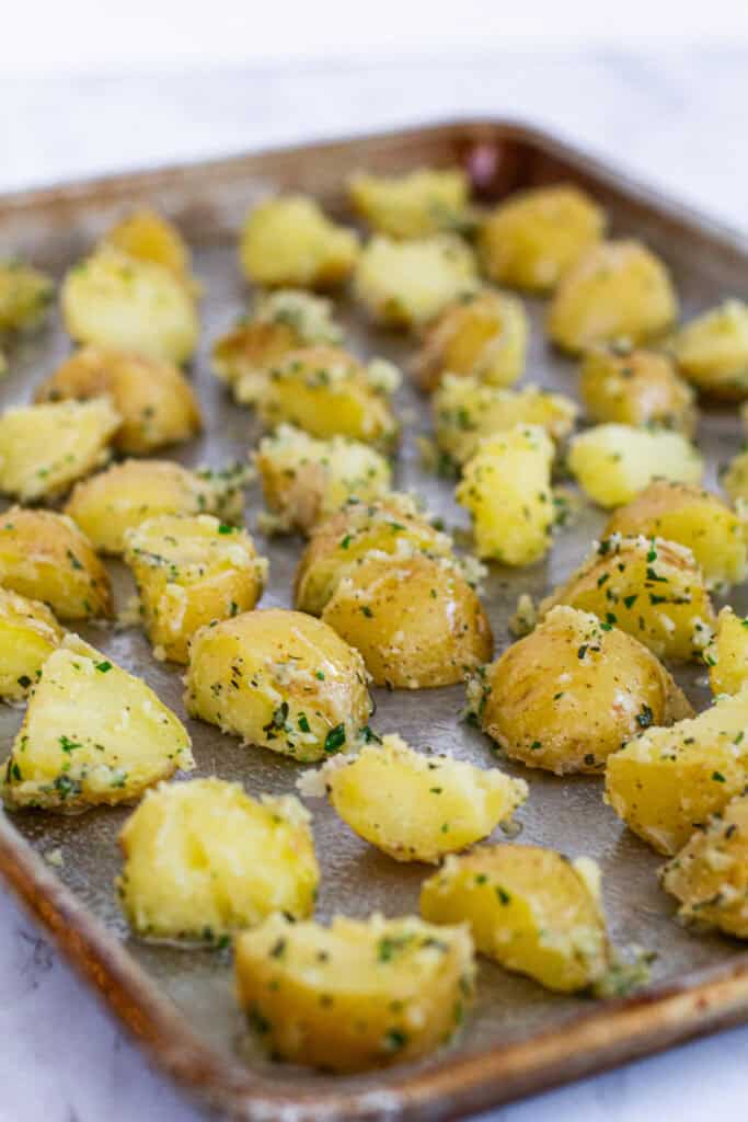 Herb butter coated yellow potatoes spread on a baking sheet before roasting in the oven.
