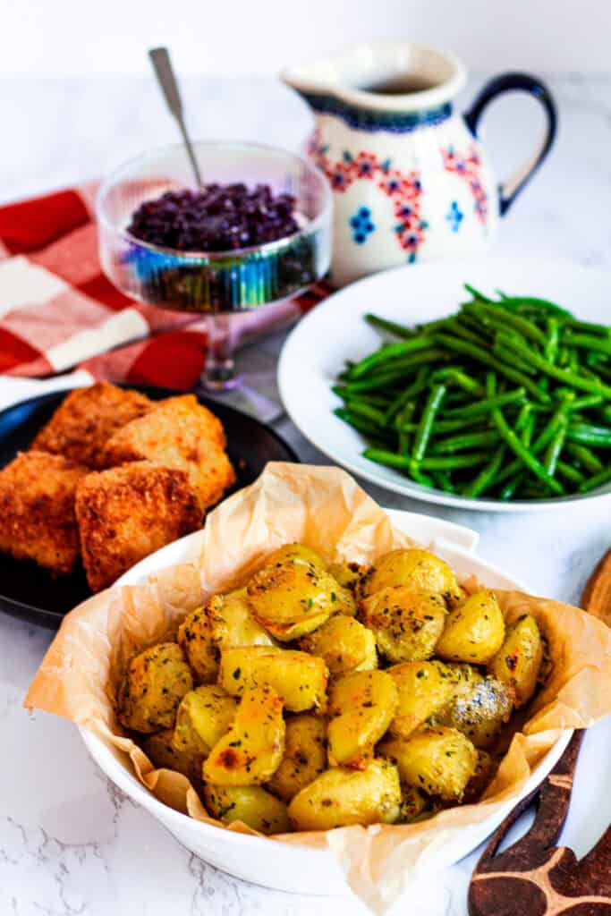 Bowl of golden herb roasted potatoes served with cranberry sauce, green beans, and mac and cheese bites for a holiday meal.