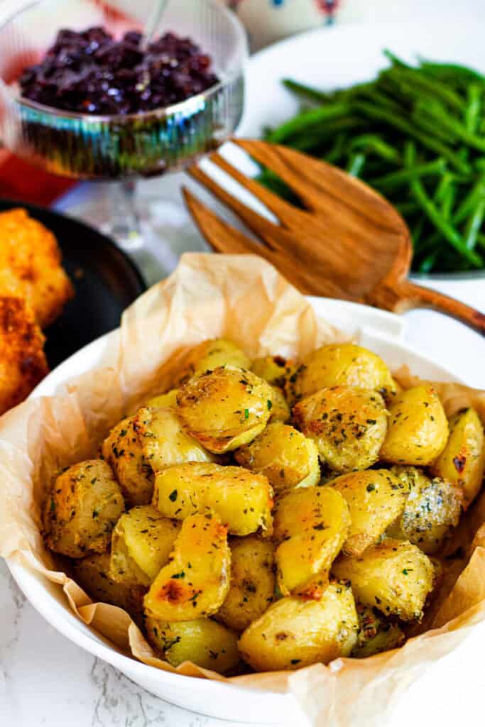 Close-up of crispy herb roasted potatoes served in a white bowl lined with parchment paper.