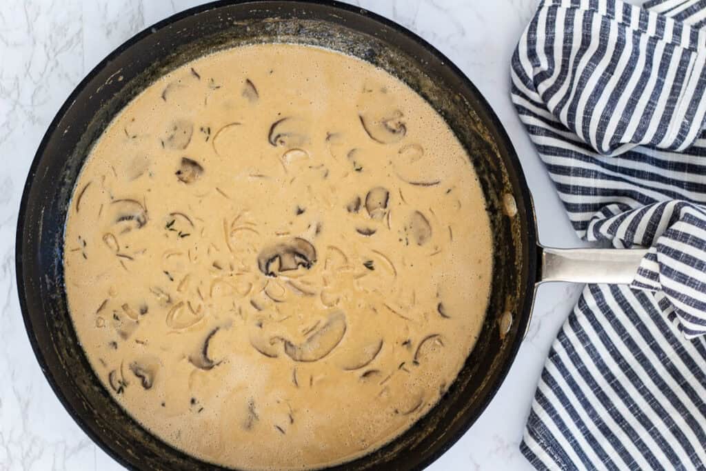 Creamy mushroom marsala sauce thickening as it reduces in a skillet.