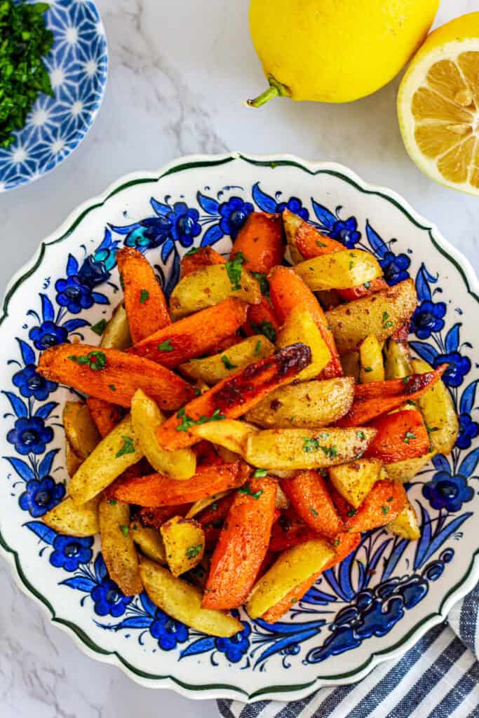 Overhead view of Moroccan roasted carrots and parsnips in a patterned bowl with fresh parsley garnish