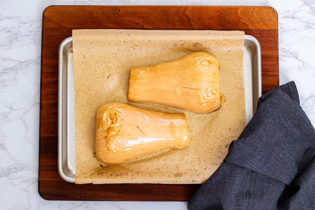 Two roasted butternut squash halves placed face down on a parchment-lined baking sheet.