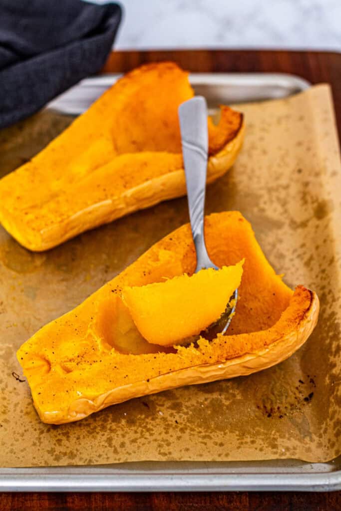 Roasted butternut squash halves on a baking sheet with a spoon scooping out the tender, golden flesh.