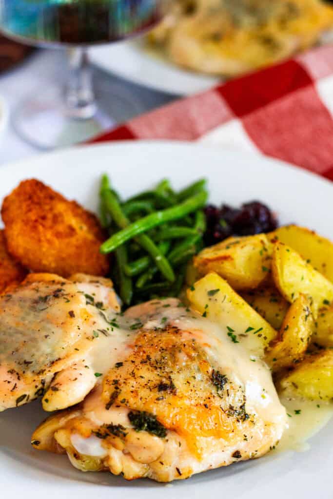 Juicy Thanksgiving chicken thighs with herb butter and gravy served alongside roasted potatoes, green beans, cranberry sauce, and mac and cheese bites.