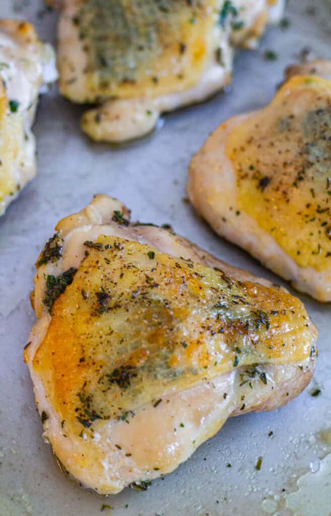 Golden roasted chicken thighs seasoned with fresh herb butter on a sheet pan, perfect for a small Thanksgiving meal.