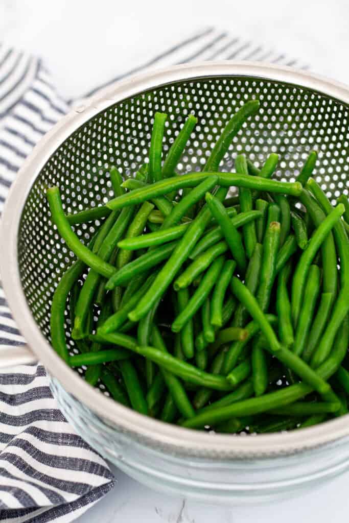 Frozen green beans rinsed and drained in a metal colander before sautéing