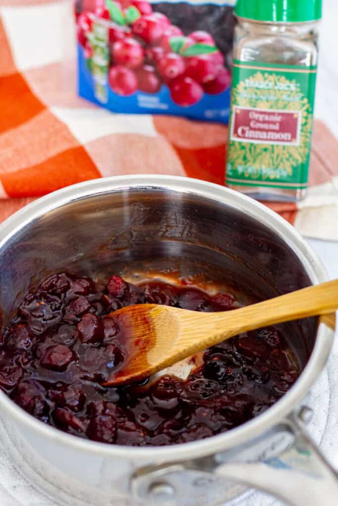 Cranberry mixture thickening in a saucepan with ground cinnamon in the background.
