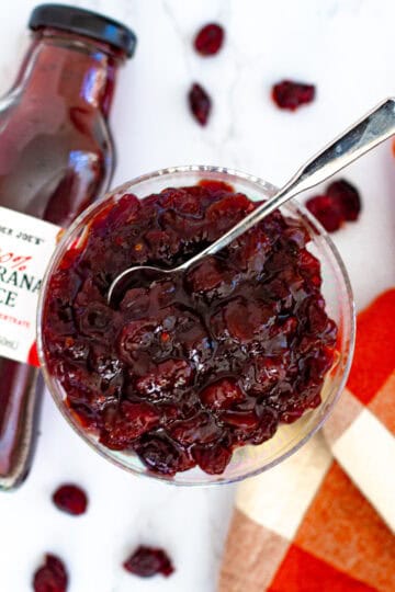 Thick and glossy cranberry sauce with dried cranberries served in a glass bowl, spoon ready for serving.